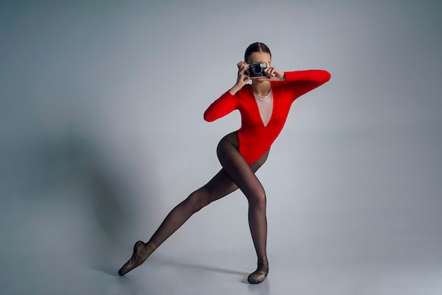 Foto retrato de uma jovem bailarina em um terno vermelho posando com uma câmera em um estúdio de fotos