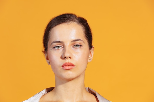 Retrato de uma jovem bonita atentamente na câmera posando isolada sobre o estúdio amarelo