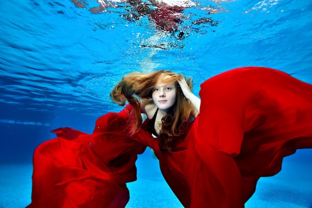 Foto retrato de uma jovem bonita com cabelo comprido que nada e joga debaixo d'água com um pano vermelho