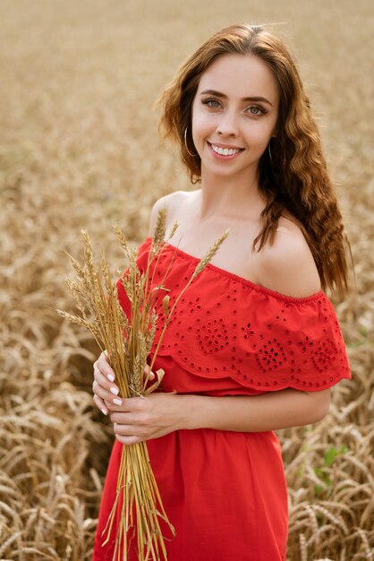 Retrato de uma jovem bonita com cabelo encaracolado em um vestido vermelho em um campo de trigo