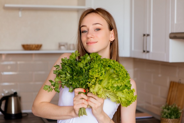 Retrato de uma jovem bonita com folhas de alface na cozinha