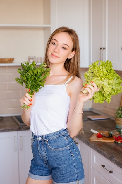 Retrato de uma jovem bonita com folhas de alface na cozinha