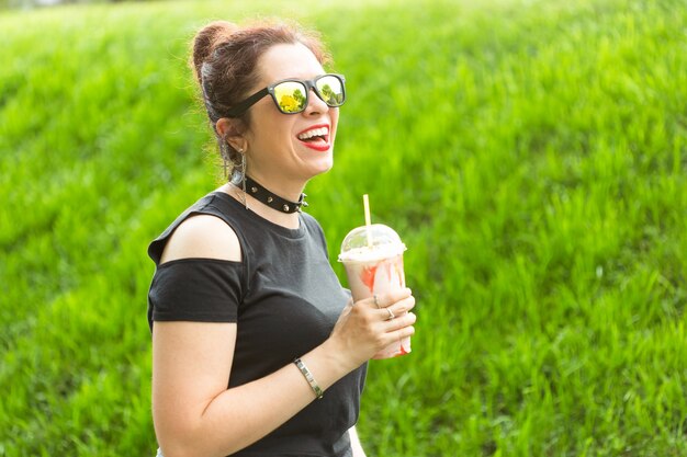 Retrato de uma jovem bonita com roupas punk e óculos com um milkshake nas mãos