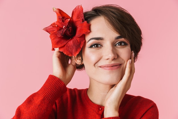 Retrato de uma jovem bonita com um vestido vermelho de pé isolado, posando com uma flor