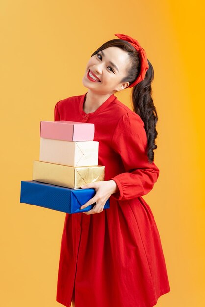 Retrato de uma jovem bonita de vestido vermelho segurando a pilha de caixas de presentes isoladas sobre fundo laranja