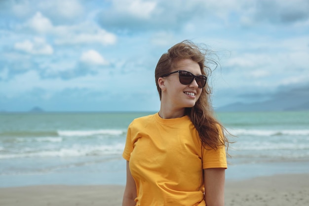 Retrato de uma jovem bonita e despreocupada, feliz e positiva, de cabelos ruivos, aproveitando as férias de verão na praia do mar, em um país tropical exótico em óculos de sol