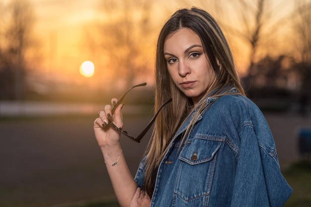 Retrato de uma jovem bonita e elegante com óculos de sol na mão ao pôr do sol