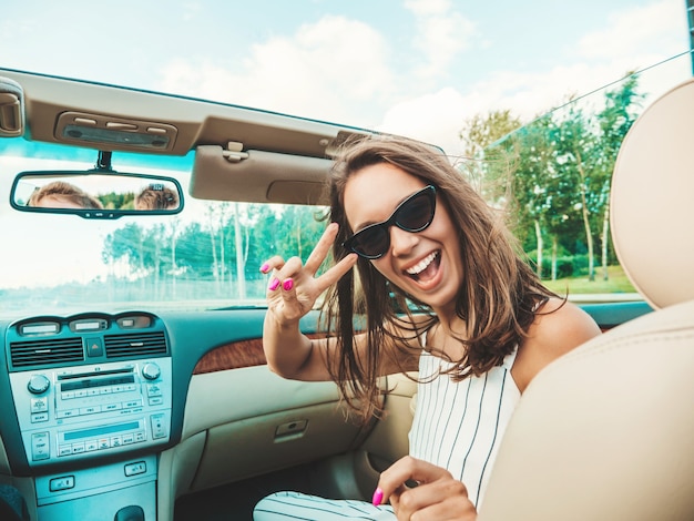 Retrato de uma jovem bonita e sorridente hipster feminina em um carro conversível