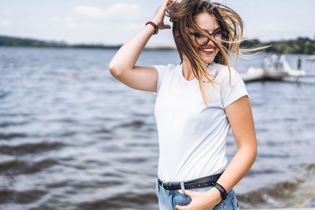 Retrato de uma jovem bonita em copos elegantes. Garota em camiseta branca posando no fundo da paisagem do lago