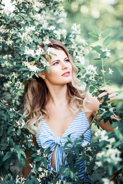 Retrato de uma jovem bonita em um fundo de flores na natureza. Garota feliz, cercada por flores