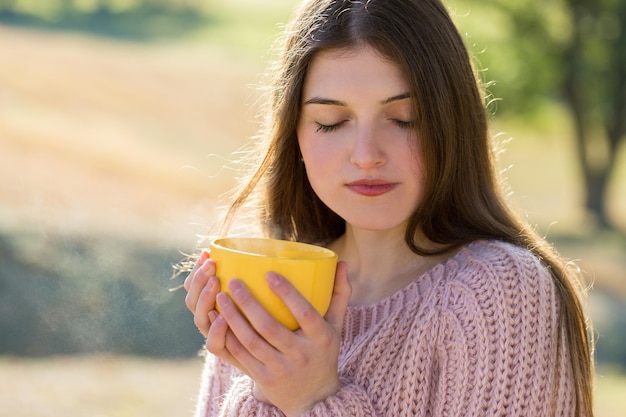 Retrato de uma jovem bonita na camisola de malha elegante em pé na floresta de outono dourada em dia ensolarado Hora de relaxar e tomar um café