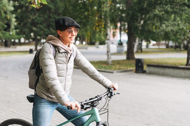 Retrato de uma jovem bonita na moda em boné e óculos de sol em bicicleta no dia ensolarado de outono no parque da cidade