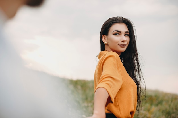 Retrato de uma jovem bonita olhando para o namorado ao ar livre. Jovem morena de cabelos escuros andando de mãos dadas com seu homem.