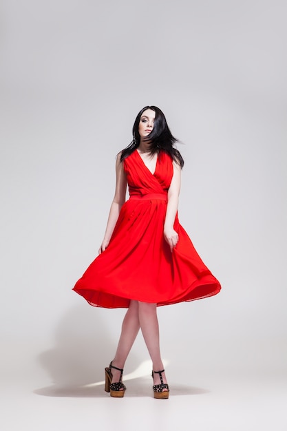 Retrato de uma jovem bonita se torcendo em um vestido vermelho enquanto olha para a câmera.