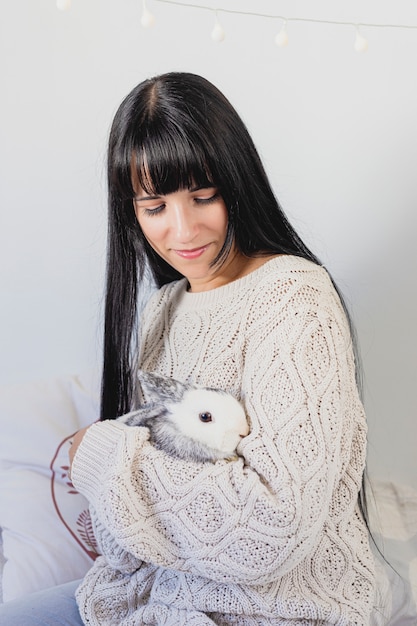 Retrato de uma jovem bonita, segurando um coelho com roupa de inverno em casa