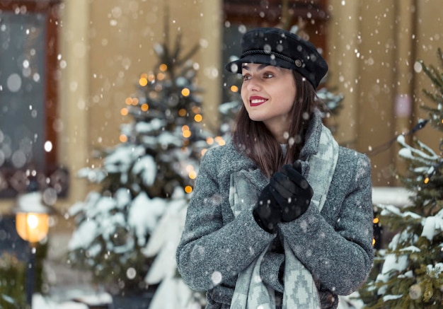 Retrato de uma jovem bonita usa chapéu preto estiloso antes do fundo da cidade de Natal na época da neve