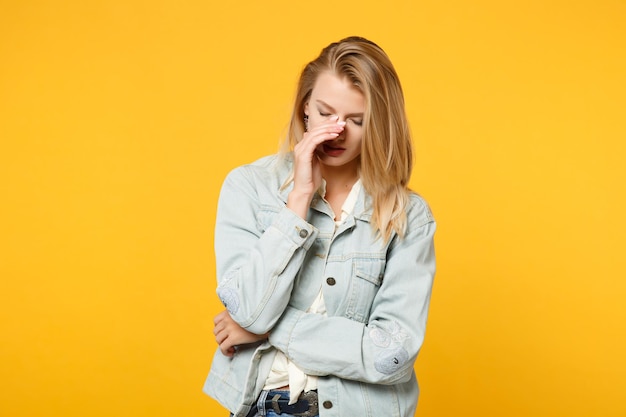 Retrato de uma jovem cansada chorando em roupas casuais jeans, mantendo os olhos fechados, colocando a mão no nariz isolado no fundo da parede laranja amarela no estúdio. Conceito de estilo de vida de pessoas. Mock up espaço de cópia.