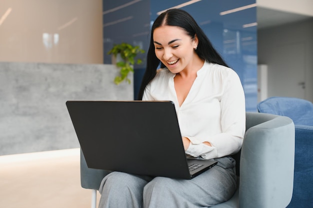 Retrato de uma jovem caucasiana animada comemorando o sucesso enquanto está sentado com o laptop em casa ou no escritório moderno Feliz freelancer feminina trabalhando no espaço de coworking