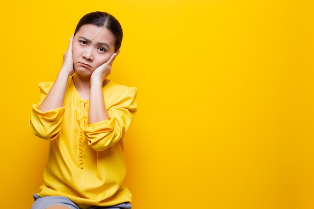 Foto retrato de uma jovem com as mãos cobrindo as orelhas contra um fundo amarelo