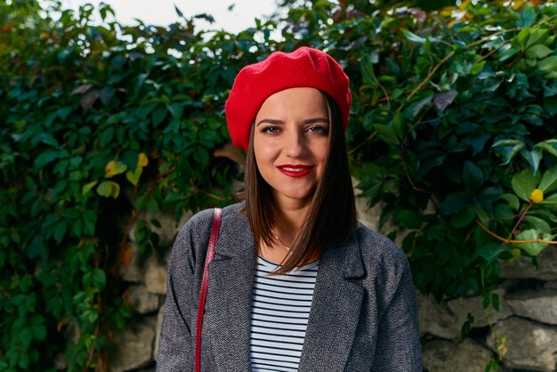 Foto retrato de uma jovem com boina vermelha contra uma cerca de pedra coberta de vegetação