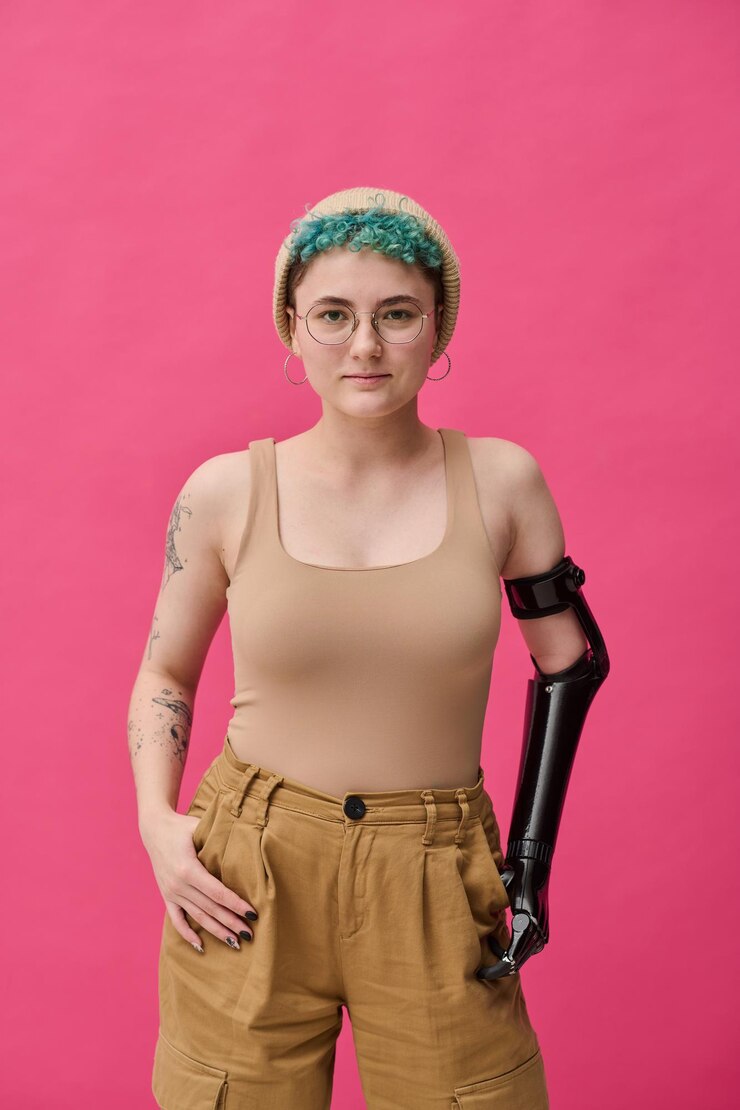 Foto retrato de uma jovem com braço protético olhando para a câmera em pé contra um fundo rosa