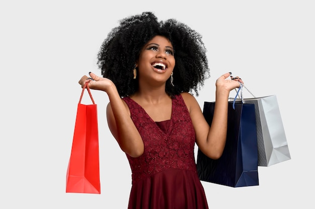 Retrato de uma jovem com penteado afro com sacolas de compras, ela sorri alegremente, com um vestido de cor vermelha, casquinha, promoção