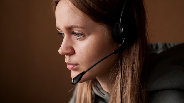 Retrato de uma jovem com um capuz e um fone de ouvido preto. Trabalhador de call center. Trabalho remoto em casa. Fotos em tons de marrom