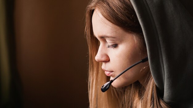 Retrato de uma jovem com um capuz e um fone de ouvido. Trabalhador de call center. Linda garota no capô. Trabalho remoto em casa. Fotos em tons de marrom