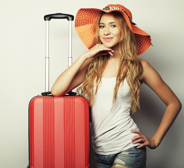 Retrato de uma jovem com um grande chapéu de palha laranja em pé com uma mala de viagem laranja