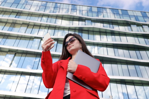 Retrato de uma jovem com um laptop e um celular no fundo de um prédio