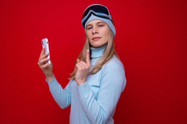 Retrato de uma jovem com um suéter e óculos de esqui com um telefone