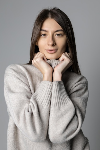 Retrato de uma jovem com um suéter em um fundo cinza Um modelo atraente olha para a câmera Beleza natural