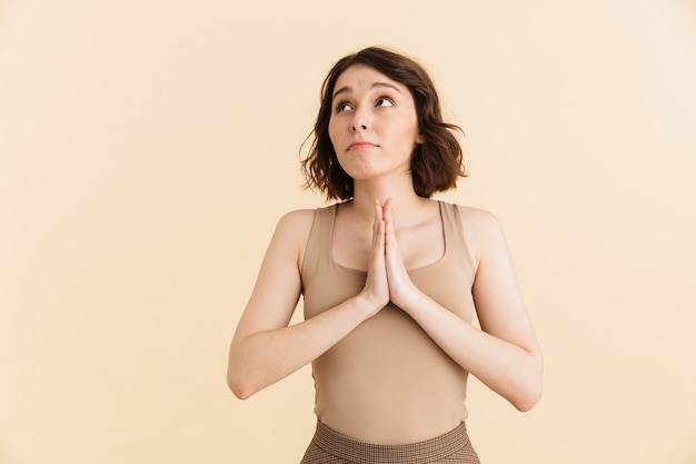 Retrato de uma jovem concentrada de 20 anos, vestida com roupas casuais, com as palmas das mãos juntas para orar isoladas