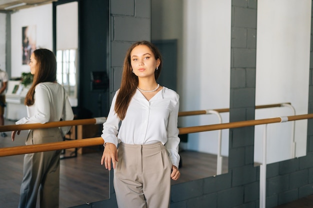 Retrato de uma jovem confiante de elegância vestindo roupas elegantes, olhando para a câmera em pé na sala com espelho