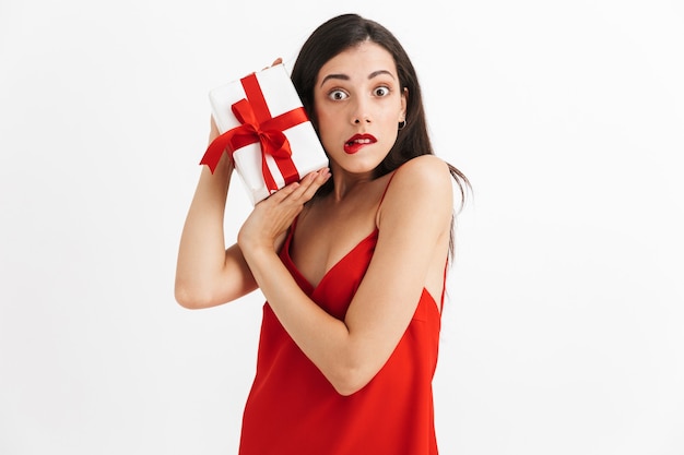 Retrato de uma jovem confusa em um vestido vermelho segurando uma caixa de presente isolada