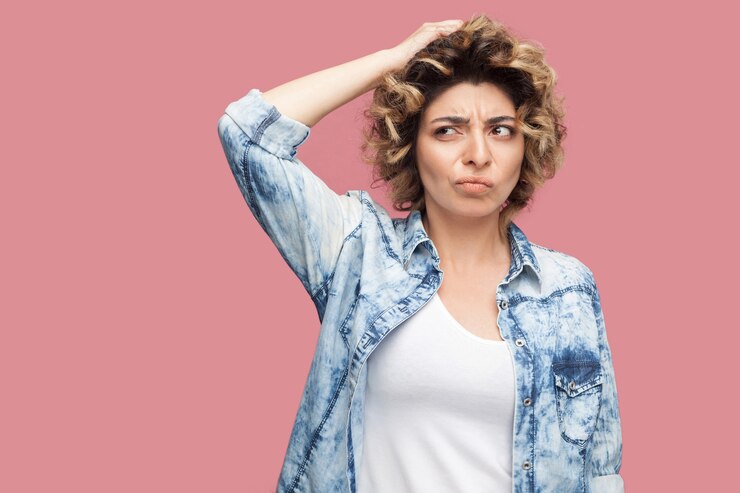 Foto retrato de uma jovem confusa pensativa com penteado encaracolado em pé casual de camisa azul coçando a cabeça e pensando o que fazer. tiro de estúdio interno, isolado no fundo rosa.