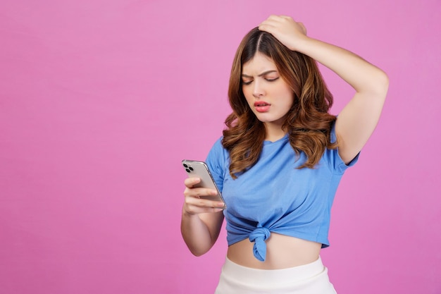 Retrato de uma jovem confusa vestindo camiseta casual usando smartphone isolado sobre fundo rosa