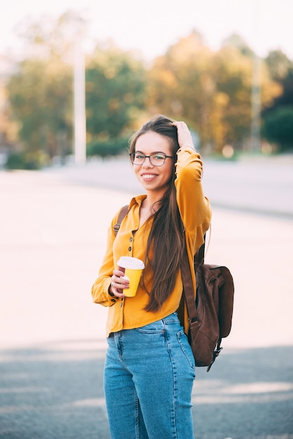 Retrato de uma jovem de óculos no parque segurando um copo de bebida quente