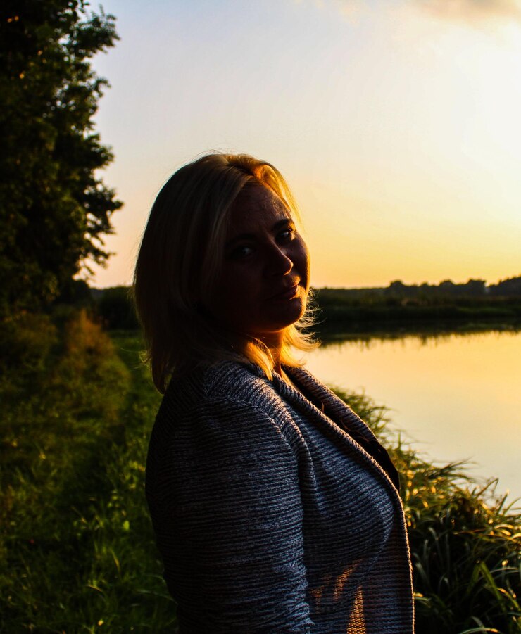 Foto retrato de uma jovem de pé ao lado do lago contra o céu durante o pôr-do-sol
