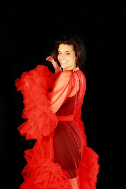 Foto retrato de uma jovem de pé contra fundo preto em uma túnica vermelha