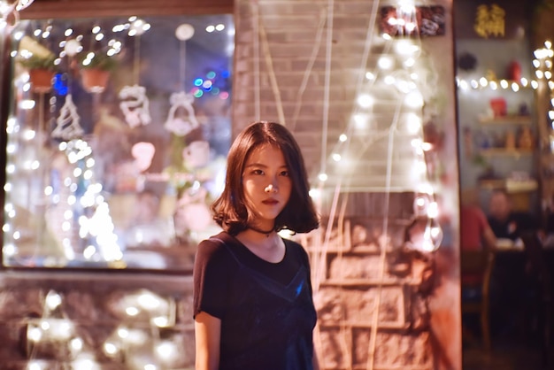 Foto retrato de uma jovem de pé contra uma parede iluminada à noite