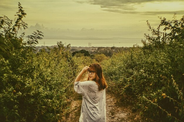 Foto retrato de uma jovem de pé junto a plantas contra o céu