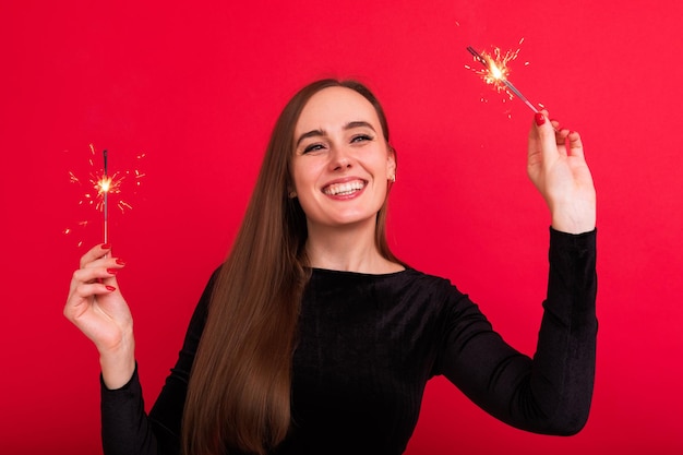 Retrato de uma jovem de vestido preto segurando faíscas nos feriados de Natal do estúdio