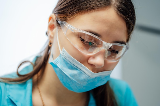 Retrato de uma jovem dentista em máscara cirúrgica e óculos de segurança Rosto de beleza de um médico ou enfermeiro usando máscara protetora e óculos na clínica Closeup