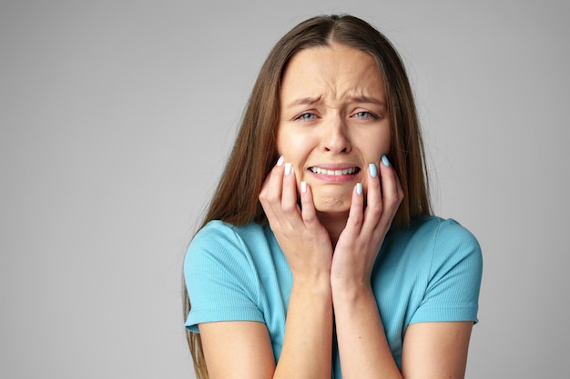 Foto retrato de uma jovem descontentada e chateada começando a chorar em fundo cinzento