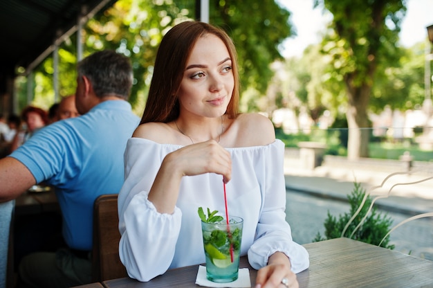 Retrato de uma jovem deslumbrante, posando com mojito cocktail no café ao lado do parque.