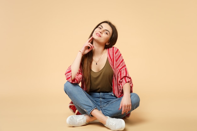 Retrato de uma jovem deslumbrante sorridente em roupas casuais, sentado, olhando a câmera isolada no fundo da parede bege pastel no estúdio. emoções sinceras de pessoas, conceito de estilo de vida. simule o espaço da cópia.