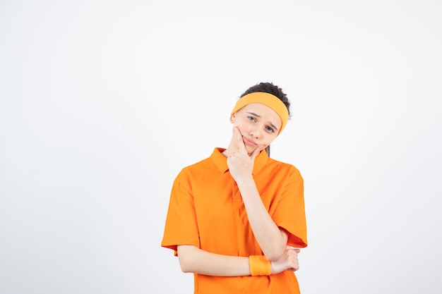 Retrato de uma jovem desportista em roupa laranja, pensando em branco.