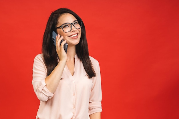 Retrato de uma jovem e alegre empresária vestindo casual usando falando no celular isolado sobre fundo vermelho