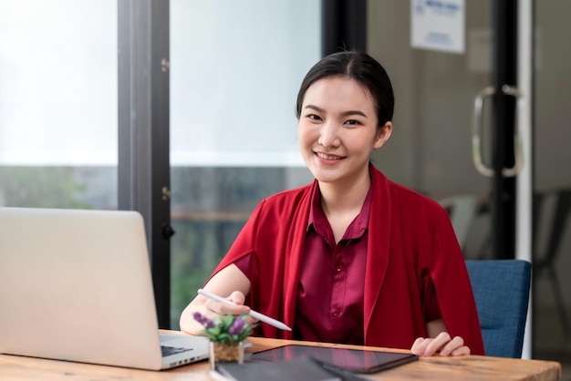 Retrato de uma jovem e bela empresária asiática sorridente sentada com um computador portátil olhando para a câmera no escritório
